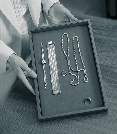 Frauanhände halten eine Schatulle mit einer Damenuhr, Armband, Halskette, Ohrring und Fingerring aus Gold.