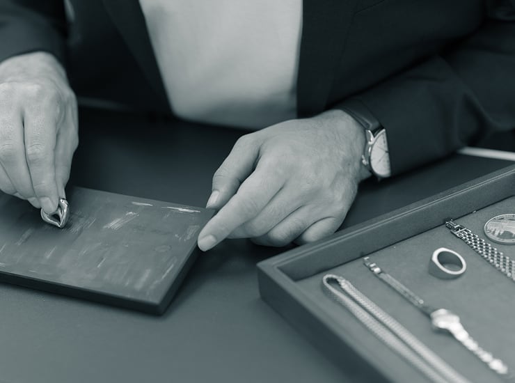 Degussa-Mitarbeiter prüft Schmuckstücke aus Silber auf einem Prüftisch mit Werkzeug und Lupe