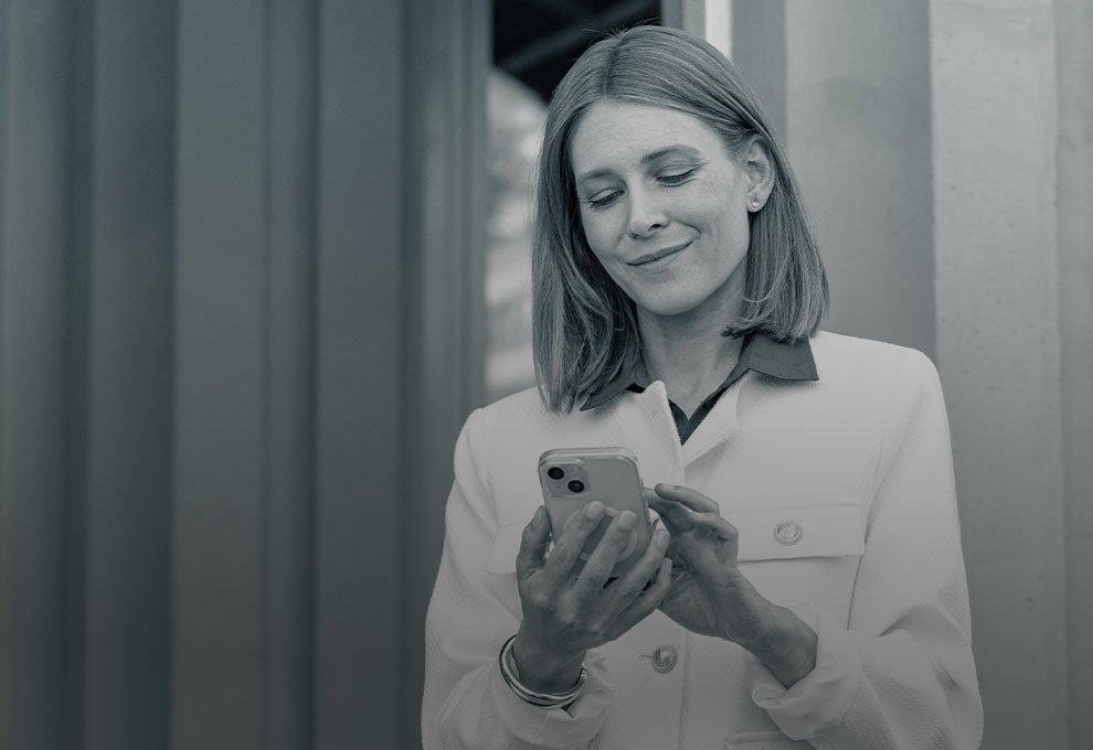 Frau in heller Kleidung nutzt ihr Smartphone, um Goldpreise oder Anlagerechner abzurufen