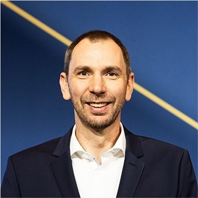 Mark Sommer, der CFO von Degussa, steht lächelnd vor einem königsblauen Hintergrund