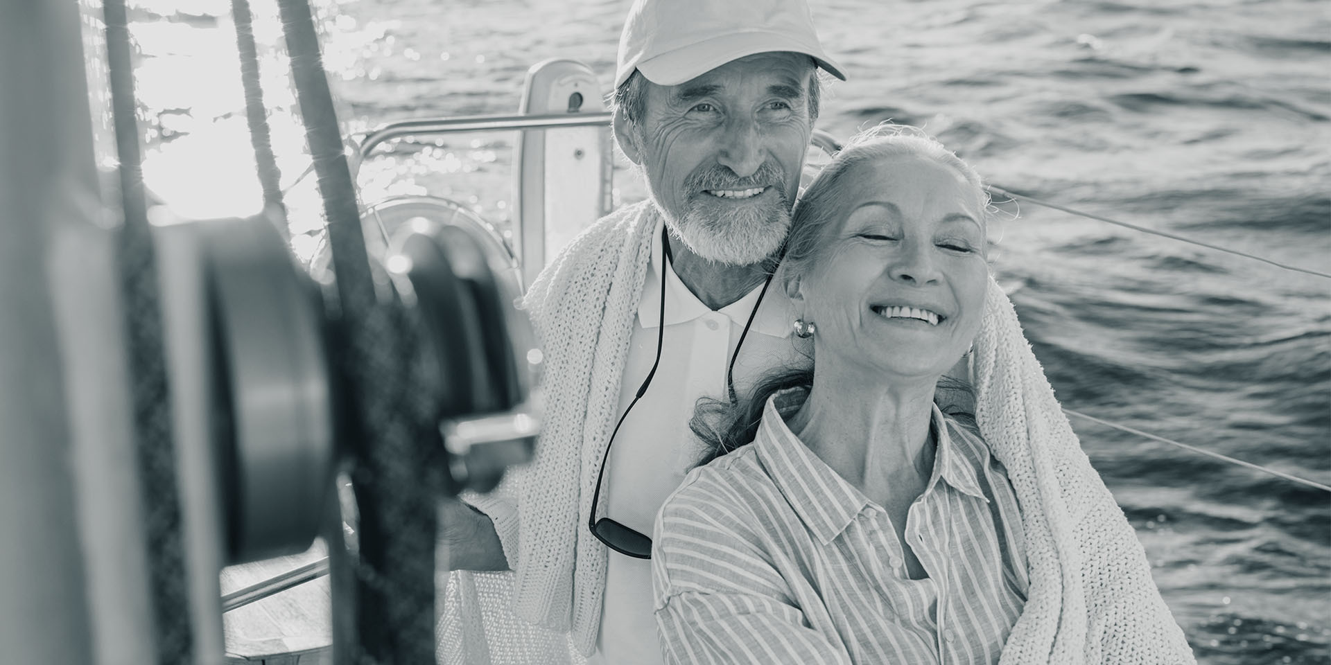 Älteres Paar sitzt lachend auf einem Segelboot und genießt die Fahrt auf dem Meer.
