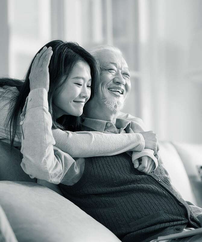 Junge Frau umarmt lächelnd ihren Großvater auf dem Sofa