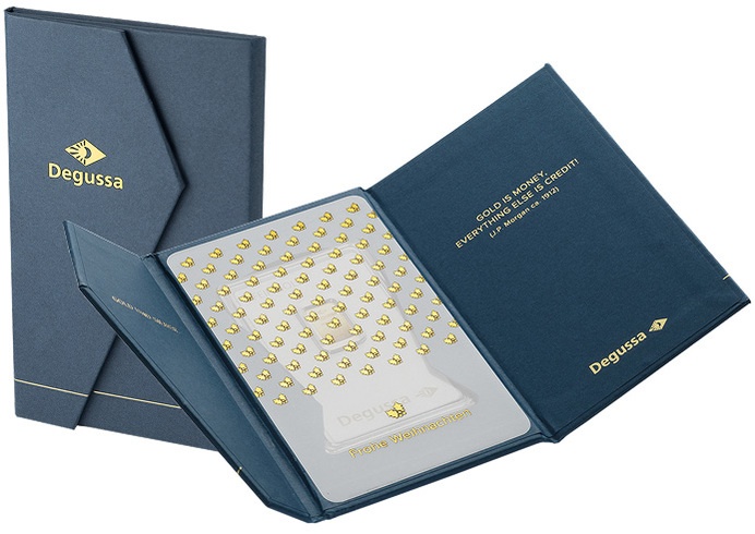 Aufgeklapptes dunkelblaues Degussa-Geschenketui mit Goldbarren und Anlasskarte mit geprägtem, goldenem Schriftzug „Frohe Weihnachten“, daneben die geschlossene Etui-Hülle mit goldenem Degussa-Logo.