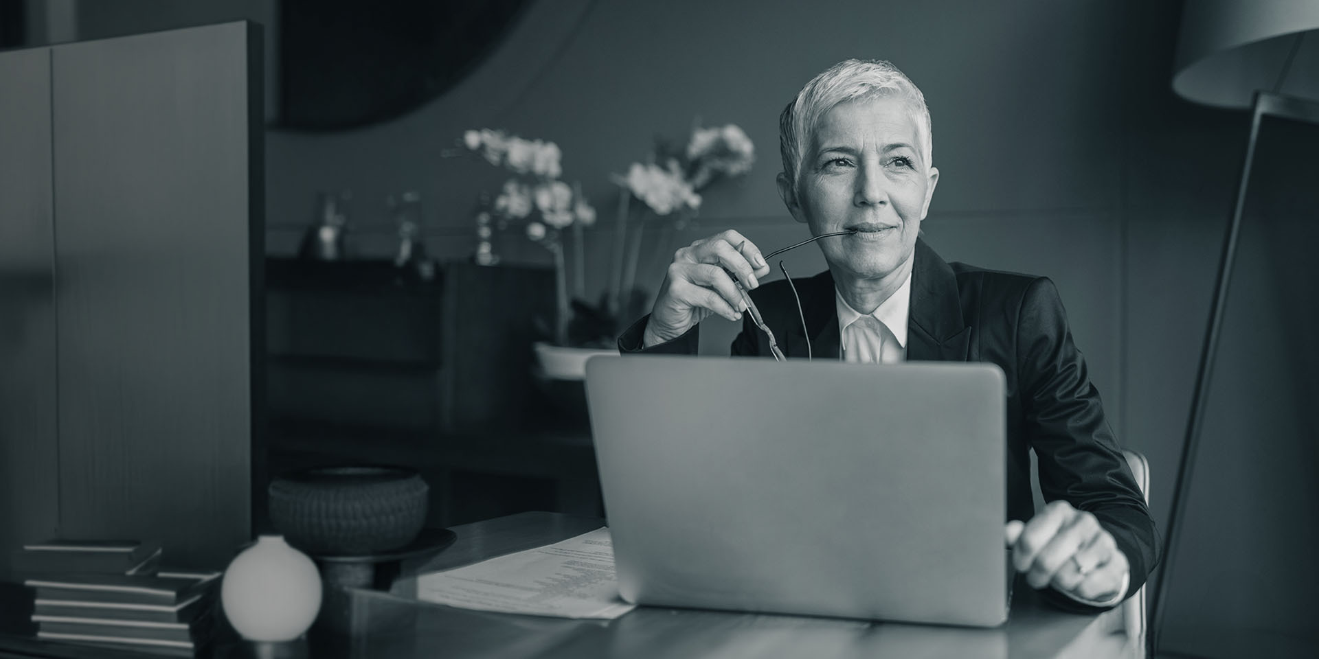 Geschäftsfrau mit weißen kurzen Haaren sitzt nachdenklich am Laptop in modernem Büro.