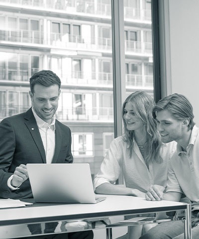 Mann in Anzug berät seine beiden Kunden mit einem freundlichen Lächeln