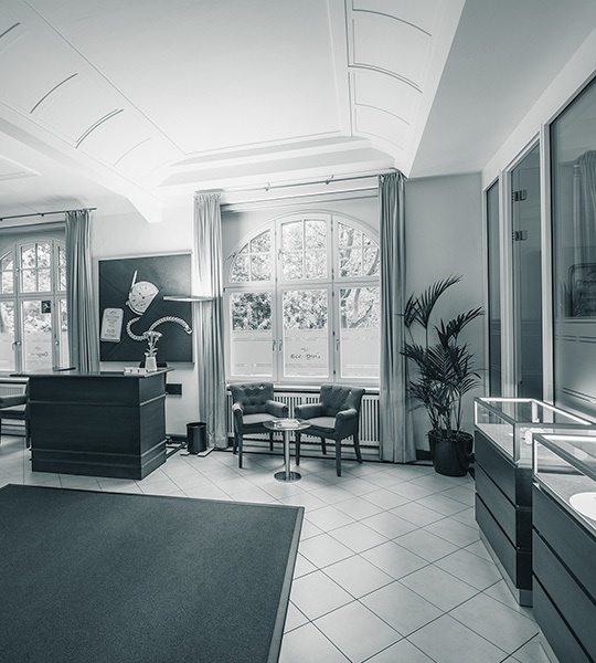 Empfangsbereichs mit dunklem Tresen, Sitzmöglichkeiten vor einem großen Rundbogenfenster und Vitrinen im Vordergrund