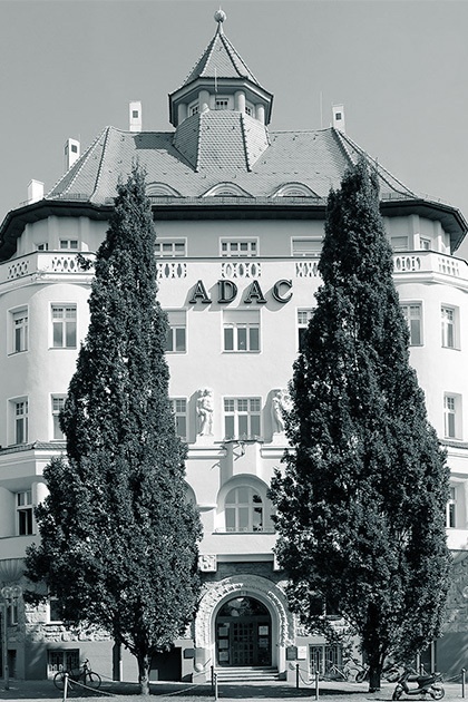 Fassadenansicht des Gebäudes in Nürnberg, in dem unter anderem auch Degussa ihren Sitz hat, mit rundem Turm und dem prominenten Schriftzug \"ADAC\", eingerahmt von zwei hohen, schlanken Bäumen