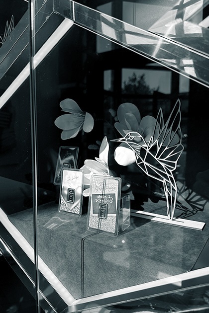 Nahaufnahme einer Schaufensterauslage mit kleinen Goldbarren in Verpackungen und Dekorationen wie stilisierten Blumen und einem Kolibri