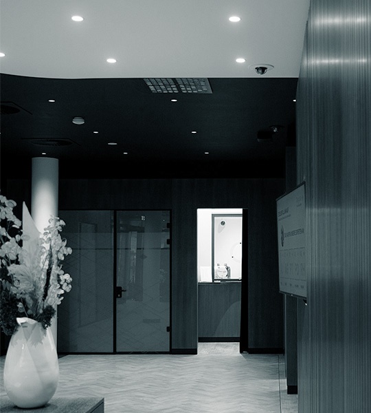 Moderner Empfangsbereich mit dunkler Decke, Holzboden, einer großen Bodenvase und Glastüren, die zu Beratungsräumen führen