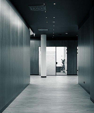 Flur mit dunkler Wandverkleidung, hellem Holzboden, einer weißen Säule in der Mitte und einer Glastür am Ende