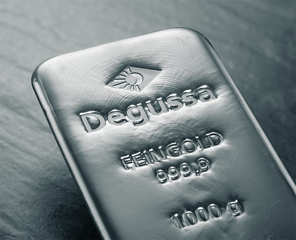 Stapelhaufen aus Degussa-Feinsilberbarren und mehreren Silbermünzen auf grauem Hintergrund