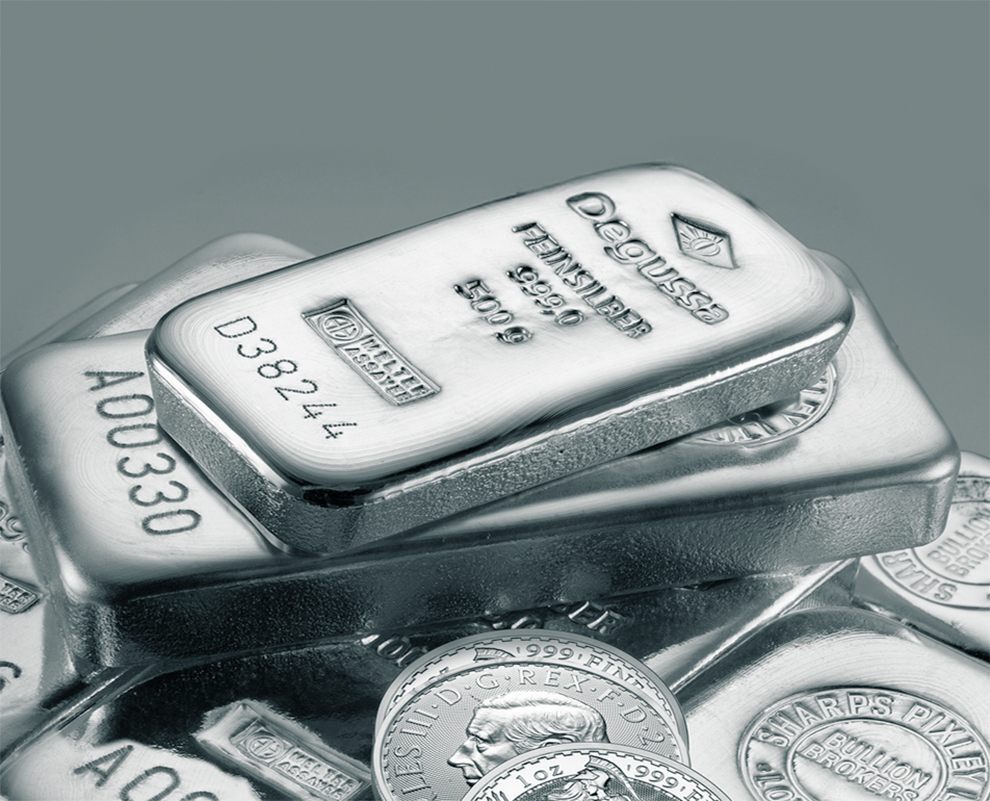 Stapelhaufen aus Degussa-Feinsilberbarren und mehreren Silbermünzen auf grauem Hintergrund