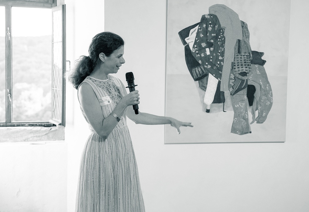 Auf einer Vernissage präsentiert eine Frau im Kleid mit Mirkofon ein Kunstwerk.