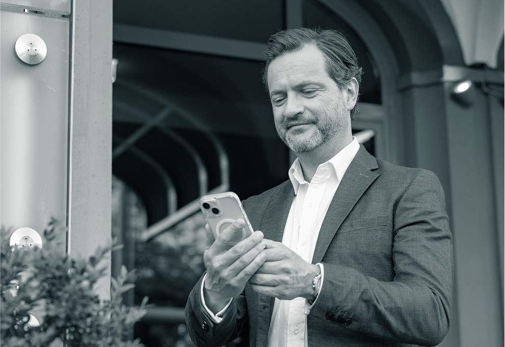 Ein Mann mittleren Alters im Anzug schaut entspannt und zufrieden auf sein Smartphone.