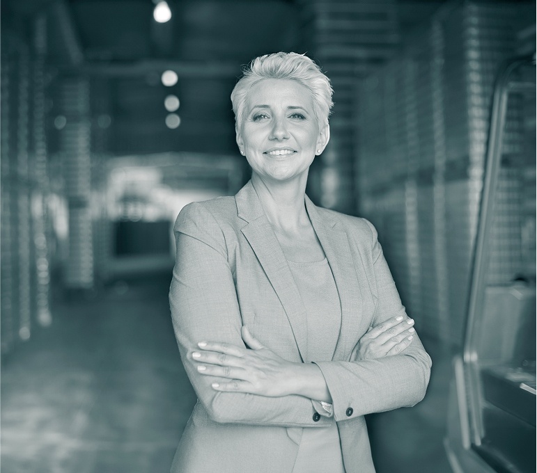 Eine smarte Frau im Business-Outfit blickt zufrieden und souverän in die Kamera mit verschränkten Armen.