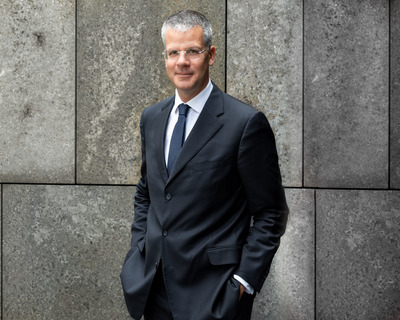 Christian Rauch, CEO von Degussa, steht lächelnd vor einem königsblauen Hintergrund