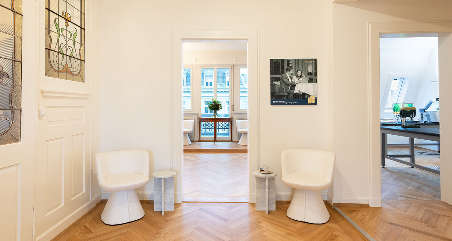 Heller Empfangsbereich des Ankaufszentrums in Zürich mit zwei Sesseln, Marmortischen und Blick in einen lichtdurchfluteten Raum mit Fensterfront