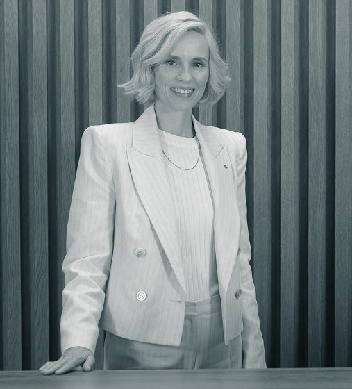 Eine freundliche Verkäuferin im schicken hellen Blazer und blonden Haaren steht am Empfangstresen einer Degussa-Niederlassung