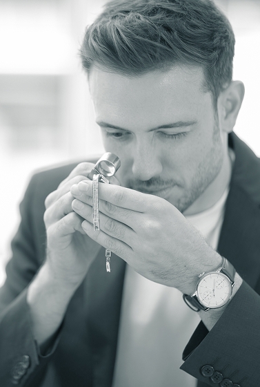 Ein junger Mann im Anzug prüft mit einer Juwelierslupe ein Goldarmband im Detail
